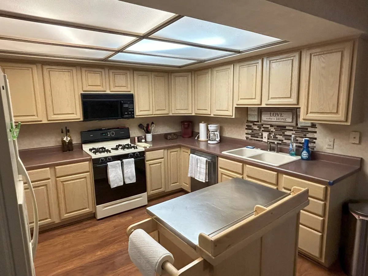 Another angle of the kitchen, this photo highlights the kitchen island, stove, sink, cabinetry, and a decorative sign that adds a personal, welcoming touch. The layout suggests efficient meal prep and a homey vibe, with thoughtful details making the kitchen both functional and charming.