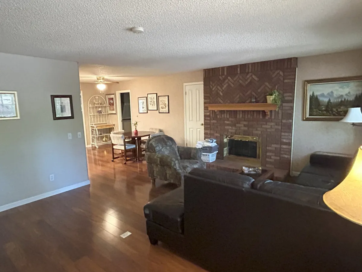 This image features a welcoming living area with a prominent fireplace, comfortable seating, and an adjacent dining table. Natural light filters into the space, accentuating the rustic charm and warmth of the interior. The arrangement encourages gatherings, relaxation, and shared moments around the fire.