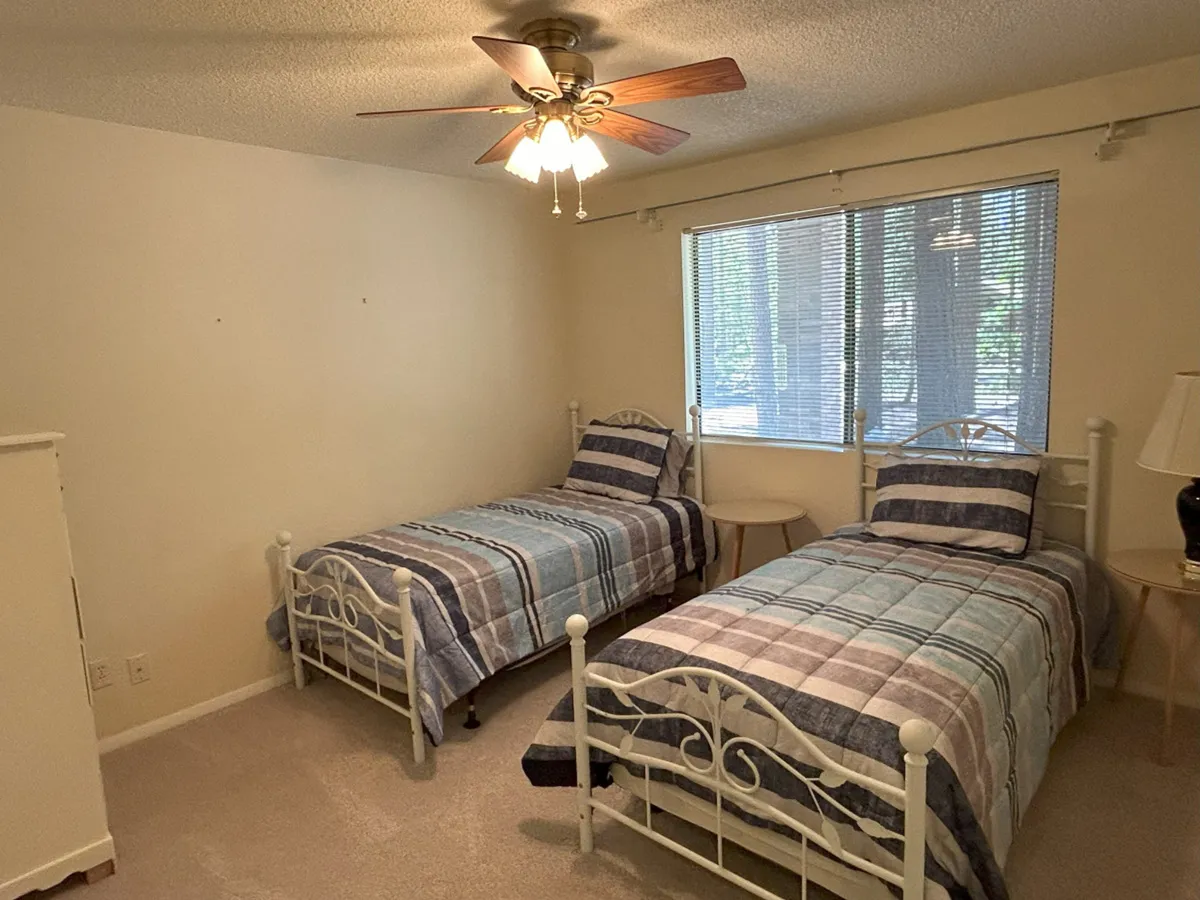 A cozy bedroom with two twin beds, a large window letting in abundant natural light, and a ceiling fan. The room feels inviting and flexible—ideal for families or groups—and suggests the shared comfort noted in the section.