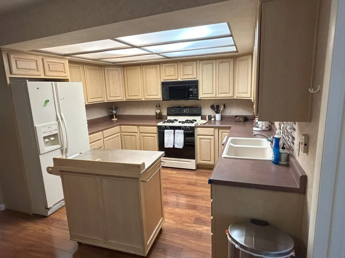 This image showcases a spacious and inviting kitchen featuring a central island, modern stove, refrigerator, and a deep sink. The scene is set for cooking and gathering, with ample counter space and cozy decor that suggests this is a hub for family activity and shared meals.