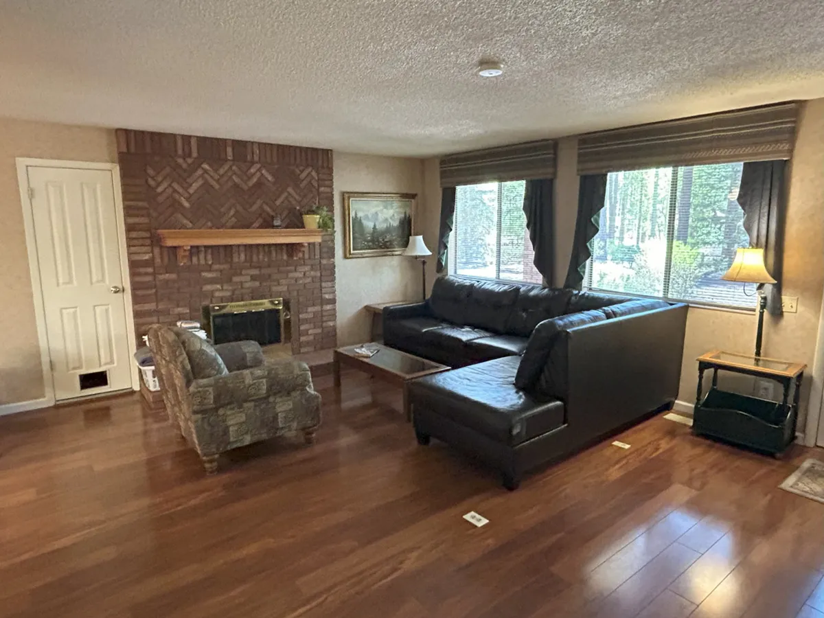 The photo captures a sunlit living area with a fireplace, a plush sofa, and large windows allowing natural light to fill the space. A coffee table sits at the center, inviting guests to unwind, socialize, or enjoy a relaxed movie night. The overall ambiance is cozy and intimate, perfect for reconnecting with loved ones.