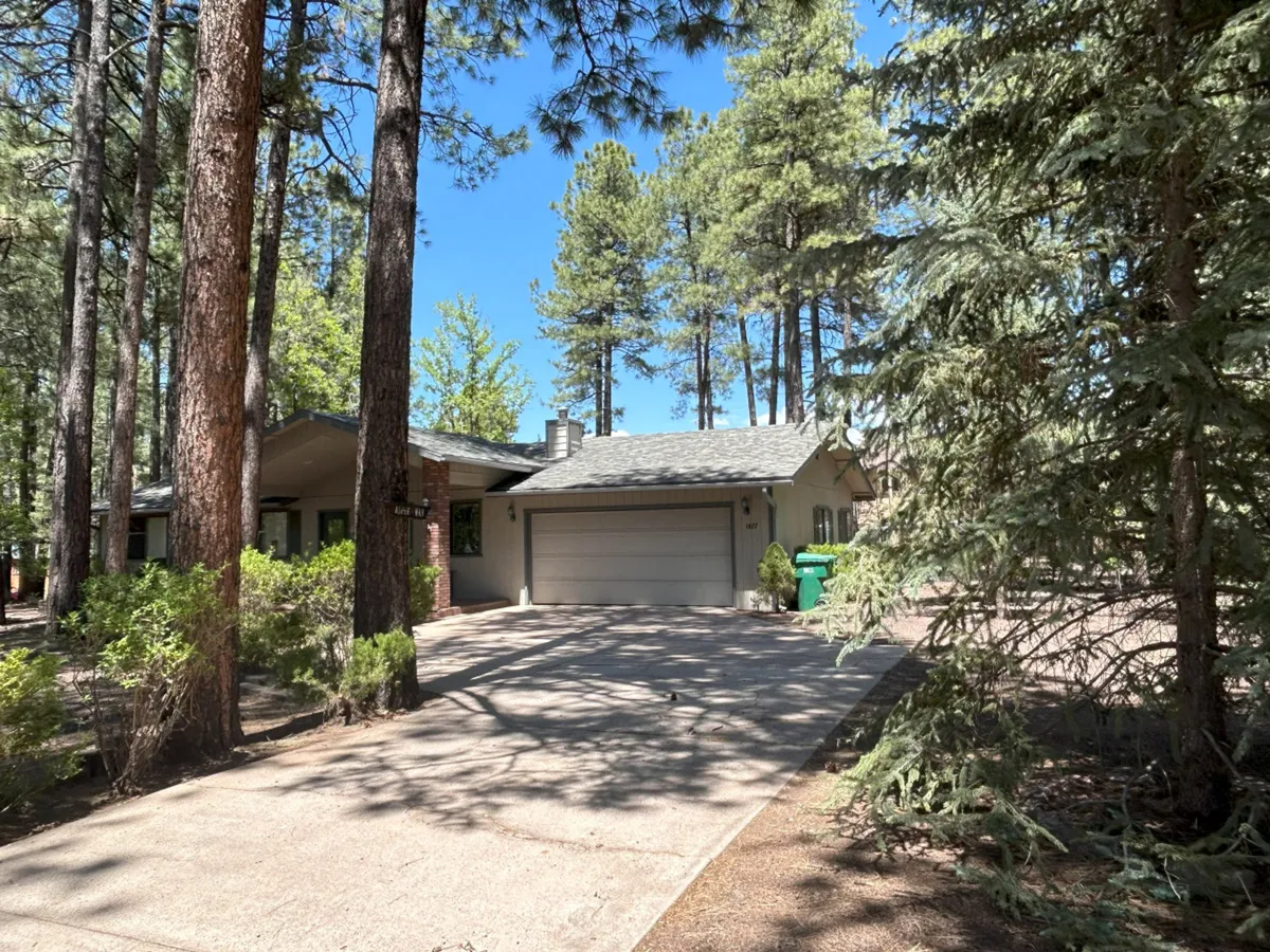 The image showcases the charming facade of a single-family house nestled among tall pine trees, with a welcoming driveway and a cozy front porch. Warm sunset light filters through the trees, casting a serene glow over the property, hinting at peaceful evenings and tranquil mornings.